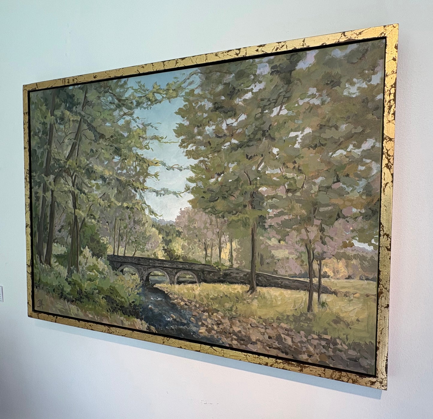 Painting of Carversville Bridge in a forested area with trees and greenery, in a gold frame, view from right angle.