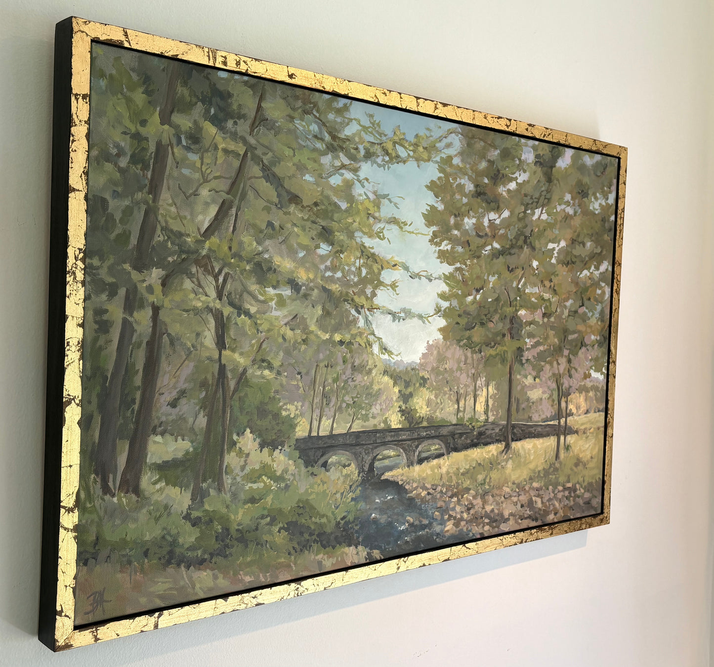 Painting of Carversville Bridge in a forested area with trees and greenery, in a gold frame, view from left angle.