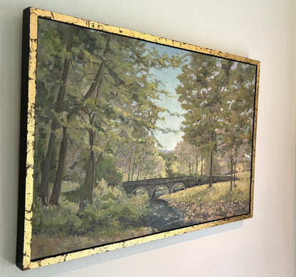 Painting of Carversville Bridge in a forested area with trees and greenery, in a gold frame, view from left angle.